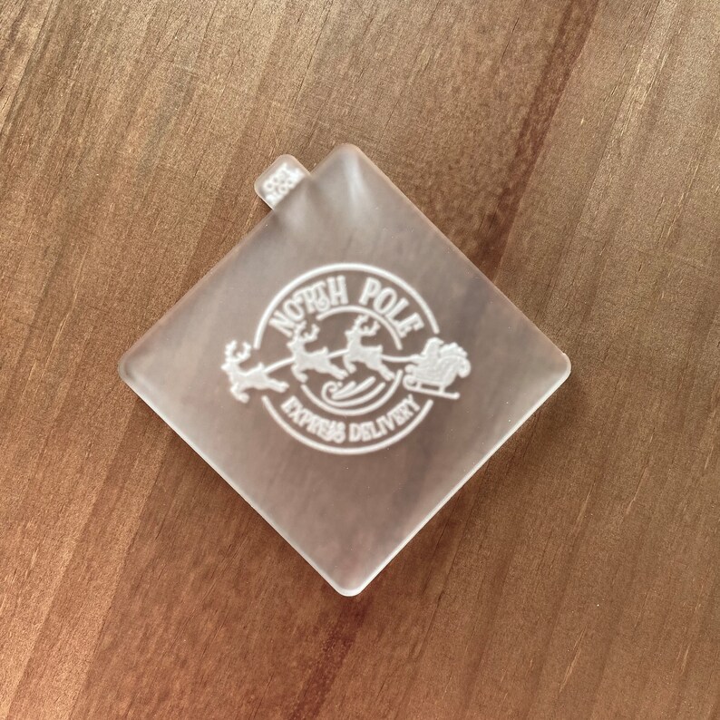 May include: A clear plastic square stamp with a white design of a sleigh pulled by reindeer with the text "North Pole Express Delivery".