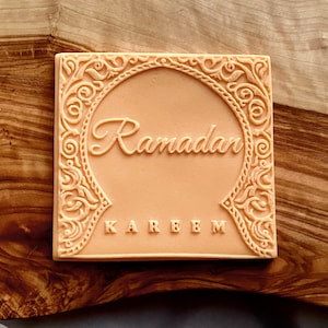 Peut inclure: Un tampon en silicone carré de couleur pêche avec une bordure ornée et les mots "Ramadan Kareem" en relief au centre.