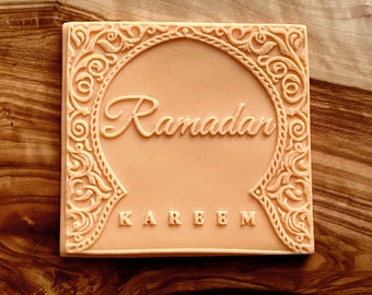 May include: A peach-colored square silicone stamp with an ornate border and the words "Ramadan Kareem" embossed in the center.