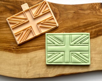 May include: A set of two cookie cutters, one peach and one green, shaped like the Union Jack flag of the United Kingdom.