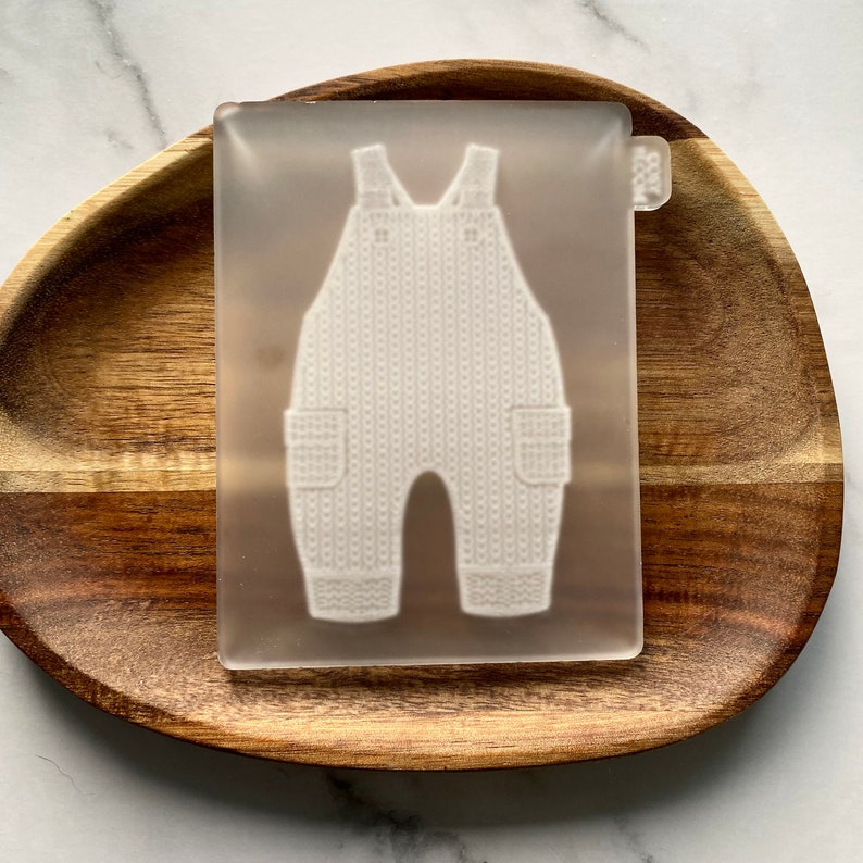 May include: A clear silicone mold for making a baby onesie. The mold is shaped like a onesie with a textured surface.