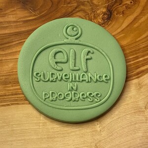May include: Green cookie cutter shaped like a surveillance camera with the text "Elf Surveillance in Progress".