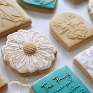 Puede incluir: Surtido de galletas de azúcar decoradas con varios diseños y lemas. Las galletas están decoradas con glaseado blanco y dorado. Algunos de los lemas en las galletas incluyen "Friends with Flowers", "Life is better with Friends", y "True Friends are never apart, Maybe in distance but never in heart".