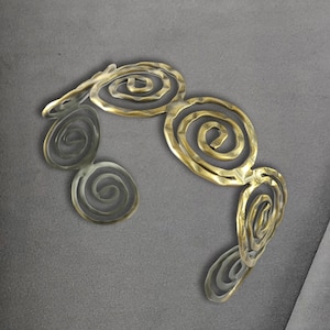 Puede incluir: Un brazalete de metal dorado y plateado con un diseño en espiral.