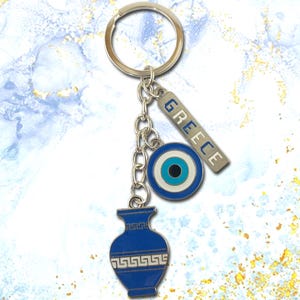 Op de afbeelding: Blauwe en zilveren Griekse sleutelhanger met een blauwe kwade oog-hanger, een blauwe vaas-hanger en een zilveren hanger met de tekst "GREECE".