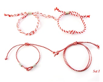 May include: Set of four red and white striped friendship bracelets with silver metal accents. The bracelets are tied with a knot and have a simple design. Set 1.
