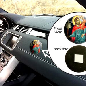 Peut inclure: Un diffuseur d'air de voiture rond avec une image d'icône religieuse sur le devant. L'image représente un homme barbu avec une auréole, tenant un enfant. L'arrière du diffuseur d'air est noir.