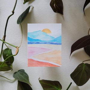 May include: Watercolour painting of a landscape with a sunset over mountains. The sky is blue and pink, and the mountains are a light blue. The sun is a bright orange.