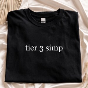 May include: Black t-shirt with white text that reads "tier 3 simp".