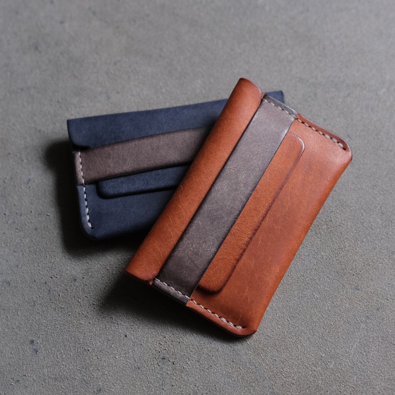 May include: Two leather wallets, one brown and one blue, with a gray leather accent. Both wallets have a stitched edge.