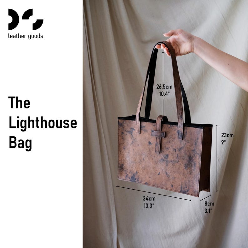 May include: A brown leather tote bag, labeled "The Lighthouse Bag," with black handles and a buckle closure. The bag measures 13.3 inches wide, 9 inches high, and 3.1 inches deep. Handle drop is 10.4 inches.