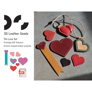 May include: A collection of heart-shaped leather goods, including a keychain, bookmark, and pendants. The items are in various shades of red, black, and green, with white stitching. The image also includes the text "DS Leather Goods" and "The Love Set".