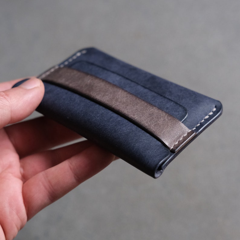 May include: A dark blue leather wallet with a brown leather strap. The wallet has a minimalist design and is perfect for carrying cards and cash.