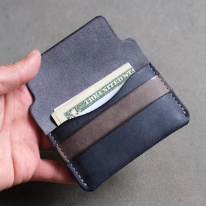 May include: A dark blue leather wallet with a brown leather accent and a single bill sticking out of the top slot.