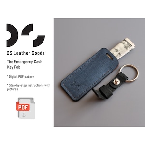 May include: A blue leather key fob with a silver key ring and a folded bill of US currency inside. The key fob is labelled "The Emergency Cash Key Fob".