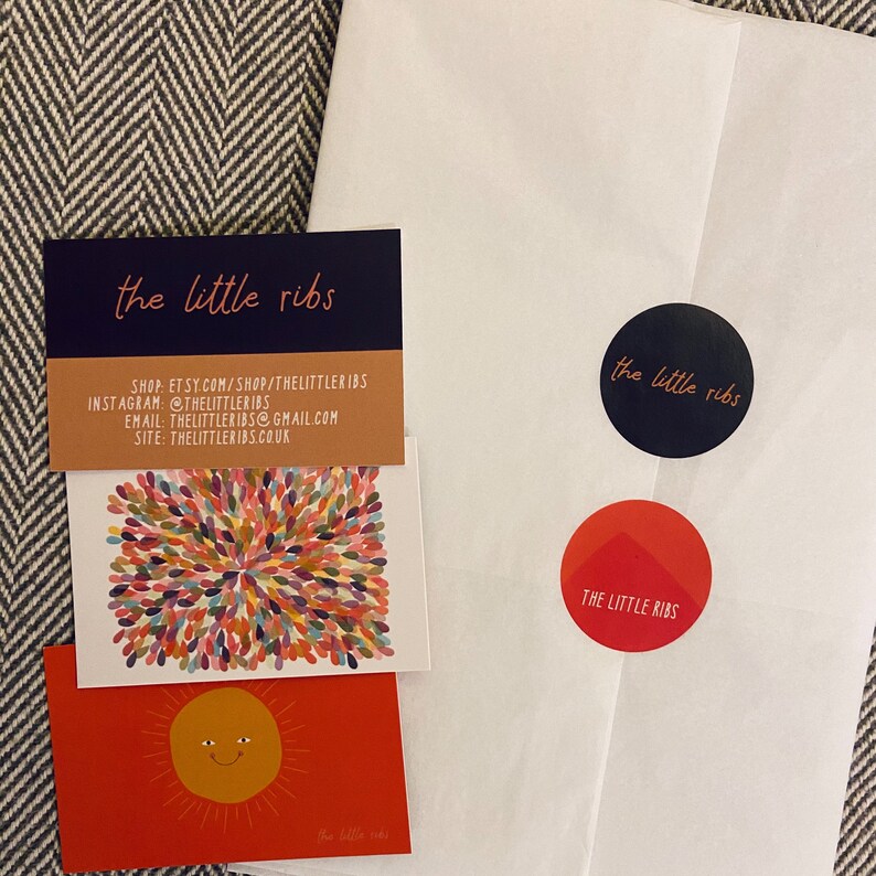 May include: A white envelope with two round stickers that say "the little ribs" in black text on a white background. The envelope also has a red sticker with the same text in white. The envelope is on a gray and white patterned surface. There are three cards with the same text in black on a white background. The text on the cards includes the shop's website, Instagram, and email address.