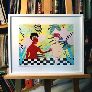 Op de afbeelding: Een ingelijste illustratie van twee vrouwen in een tropische omgeving. Een vrouw heeft een bruine huid en draagt een hoofdband. De andere vrouw heeft een witte huid en draagt een roze hoofdband. Beide vrouwen zijn naakt en staan voor een geruit patroon.