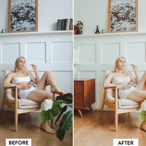 May include: A woman sits in a light-colored armchair in a white room. She is wearing a white tank top and white shorts. She is holding a phone in her hand and looking to the side. There is a plant in the foreground and a wooden side table in the background.