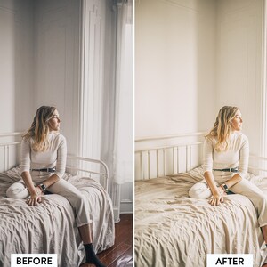 May include: A woman sits on a bed in a white room, looking out of a window. The bed has a white metal frame and a white linen duvet. The woman is wearing a white turtleneck sweater and white jeans.