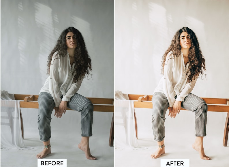 May include: A woman with long, curly brown hair sits on a wooden bench. She is wearing a white button-down shirt and striped trousers. The background is a white wall with shadows.
