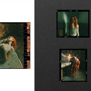 May include: A collection of three photographic film frames featuring a person with long, vibrant red hair wearing a light blue tank top. The images show the person in various poses, including lying down and standing in a dimly lit, textured environment.
