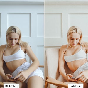 May include: A woman sits in a chair and looks down at a phone in her hands. She is wearing a white tank top and white shorts. The background is a white wall with white trim.