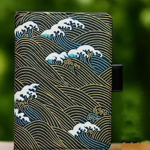 Puede incluir: Cartera negra con un patrón de olas japonesas. El diseño presenta olas con crestas blancas, detalles azules y líneas doradas sobre un fondo negro. Una correa negra asegura la cartera.