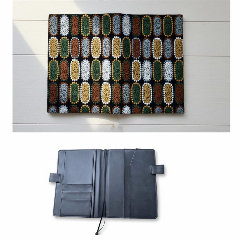 Pode incluir: Um planejador de couro preto aberto, com v&aacute;rios bolsos e um la&ccedil;o para caneta. Acima, um tecido retangular com um padr&atilde;o repetitivo de desenhos ovais coloridos em tons de verde, marrom e dourado.