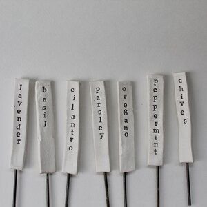 May include: White ceramic plant markers with black lettering. The markers are labeled: Lavender, Basil, Cilantro, Parsley, Oregano, Peppermint, and Chives.