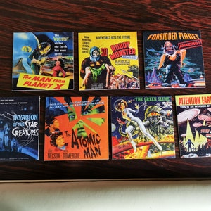 May include: A collection of vintage science fiction movie posters. The posters feature colorful illustrations of aliens, robots, and space creatures. Titles include "The Man From Planet X," "Robot Monster," and "Forbidden Planet."