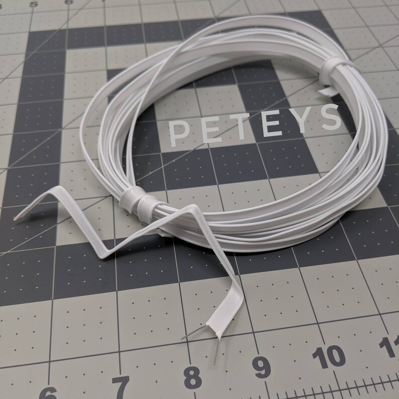 May include: A white plastic wire, coiled and ready to be used. The wire is about 1/4 inch wide and is flexible. The wire is labeled "PETEYS".