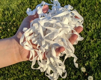 May include: A large pile of white elastic cord, also known as shoelace or string, is held in a hand. The cord is soft and flexible, and it is perfect for crafting projects.