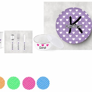 May include: A white cup with purple hearts and the name Kathryn, a spoon, fork, and knife with heart motifs and the name Kathryn, a white bowl with pink hearts and the name Sarai, a plate with purple hearts and a large letter K, and four colored circles.