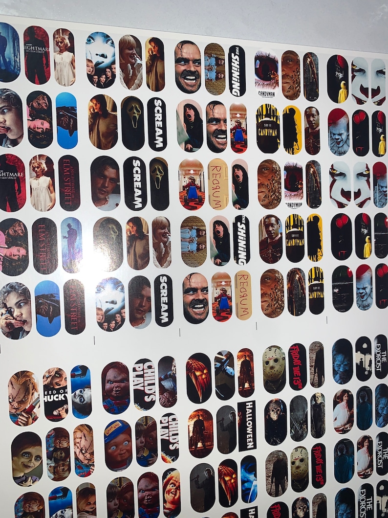 May include: A sheet of nail art transfers showcasing horror film characters and scenes. Designs include images from "The Shining," "Scream," "Child's Play," and "Friday the 13th." The transfers are oval-shaped and printed on a white background.