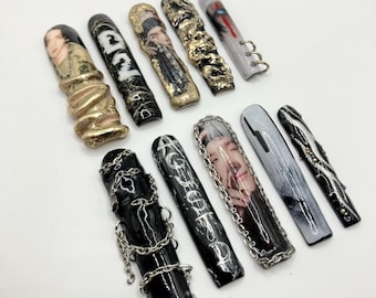 May include: Ten long, black and white false fingernails with various designs. Some nails feature chains, others have a black and white marble design, and some have a photo of a person's face. One nail has the text "AGEDEOFD" written on it.