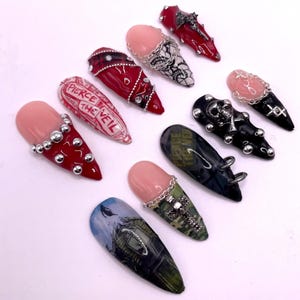 Peut inclure: Une collection d'ongles artificiels avec divers motifs. Certains ongles sont rouges avec des clous argentés, d'autres présentent du texte, et certains ont des ornements d'inspiration gothique comme des croix et des crânes. Les ongles ont une finition brillante.