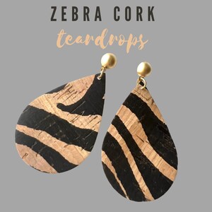 Może przedstawiać: Para kolczyków w kształcie łzy wykonanych z korka z czarno-brązowym wzorem zebry. Kolczyki mają złote sztyfty.