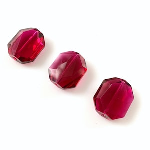 Peut inclure: Trois perles en verre rouge facettées. Les perles sont de forme octogonale et ont une finition brillante et translucide.