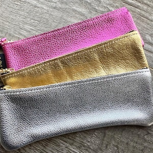 Puede incluir: Tres estuches con cremallera en plata, oro y rosa. Los estuches están hechos de un material texturizado similar al cuero.