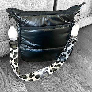 Puede incluir: Bolso de hombro acolchado negro con una correa de estampado de leopardo blanco y negro.