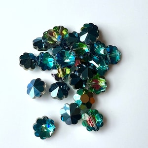 Puede incluir: Un montón de cuentas de cristal en forma de flor, iridiscentes, verde azulado y verde.