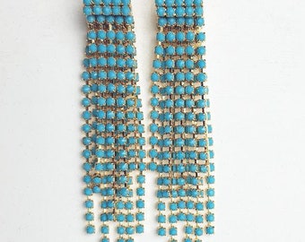 May include: A pair of long, turquoise blue, crystal-encrusted dangle earrings with gold-tone metal settings.