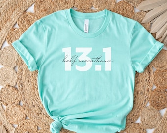 Op de afbeelding: Een turquoise blauw t-shirt met de tekst "half marathoner 13.1" in wit.