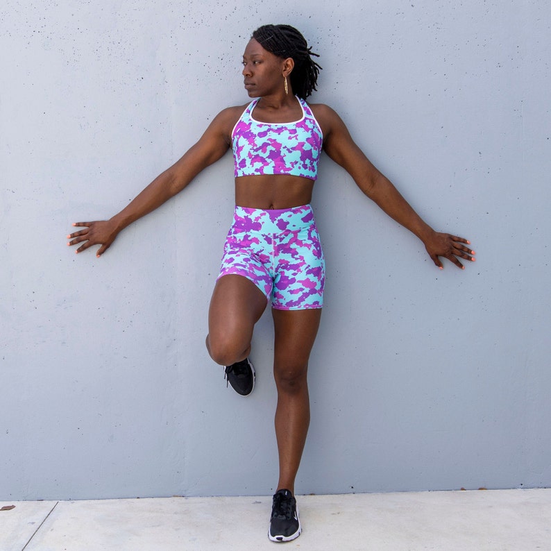 May include: A woman wearing a blue and purple camouflage sports bra and matching shorts. The outfit has a white trim.