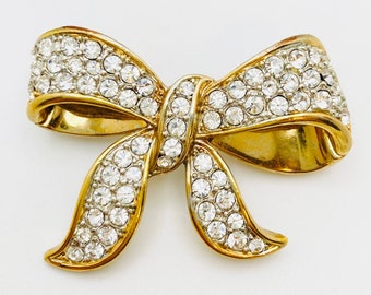 May include: A gold-toned brooch in the shape of a bow, encrusted with clear rhinestones.