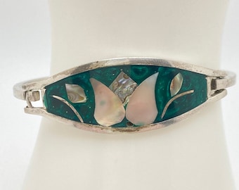 May include: Silver-toned hinged bracelet with a central rectangular design. The design features a dark green background with inlaid mother-of-pearl and abalone shell accents in a floral pattern. The bracelet is displayed on a white surface.