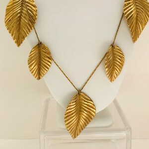 May include: A gold necklace with multiple leaf-shaped pendants. The necklace is displayed on a white stand.