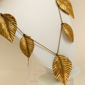 May include: A gold leaf necklace with multiple gold leaf pendants hanging from a thin gold chain.
