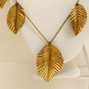 May include: A gold necklace with multiple leaf-shaped pendants. The leaves are textured and have a slightly hammered finish.