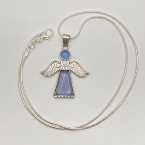 Op de afbeelding: Een zilveren ketting met een engelhanger. De engel is gemaakt van zilver en heeft een blauw glazen lichaam. De vleugels van de engel zijn versierd met een zilveren ontwerp.